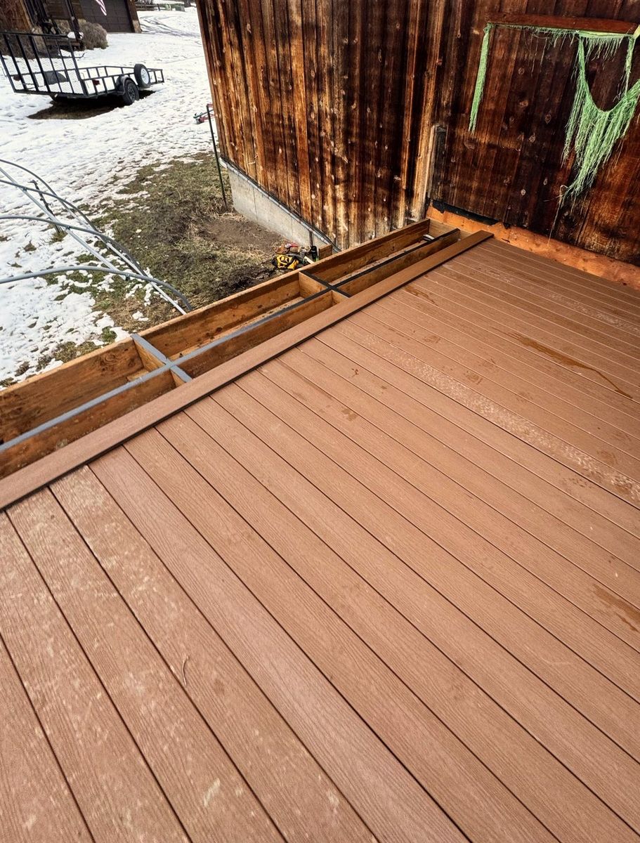 A composite deck laid up against a weathered barn board wall, with snow on the ground beyond the edge.