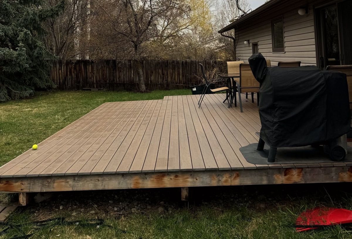 A low composite deck built off the back of a house, with a patio table and grill at one end and lawn beyond.